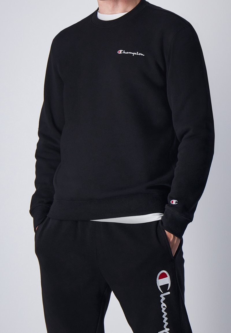 Sudadera negra con cuello redondo y logotipo bordado de "Champion". Los pantalones de chándal cuentan con un logotipo a juego y bolsillos laterales. Tejido suave.