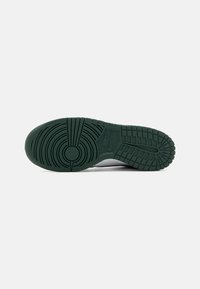 Semelle d'un sneaker Nike en caoutchouc vert foncé avec des motifs de semelle circulaires et en grille, et le logo Nike en relief au centre.