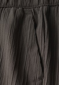 Detailní záběr na tmavě šedou texturovanou tkaninu s vertikálními záhyby a šitým elastickým pasem.