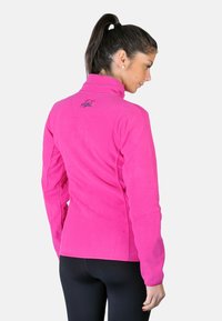 Veste en polaire de couleur rose vif avec un col haut, une coupe ajustée et des détails discrets du logo au dos. Texture lisse, manches longues.