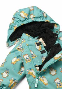 Kinderjacke in Türkis mit Pinguin-Muster. Sie verfügt über ein weiches, schwarzes Fleece-Futter und eine Kapuze. Mit Reißverschluss und Druckknöpfen zum Schließen.