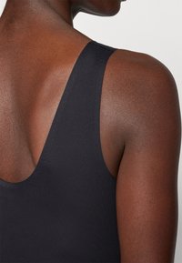 Black sleeveless garment with a low-cut back design, made of smooth fabric, featuring a seamless finish along the edges.