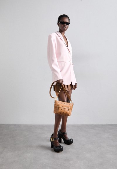 Pink blazer with gold buttons, brown pleated skirt, black chunky heeled shoes, and a tan handbag with a zipper and pattern accents.