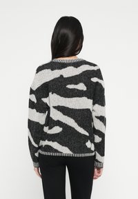 Schwarz-weiß gestreifter Pullover mit Zebramuster, strukturierter Strickmuster, rundem Ausschnitt und kontrastierendem geripptem Saum an Bündchen und Saum.