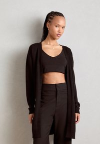 Cardigan noir en tissu doux et léger avec des manches longues et un devant ouvert ; porté par-dessus un crop top assorti et un pantalon taille haute.