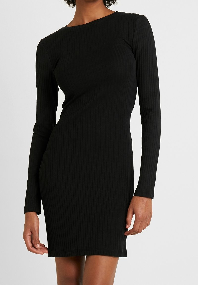 Svart ribbad långärmad klänning med en figursydd silhuett. Texturerat tyg, rund halsringning och knälång design lyfter fram dess eleganta utseende.