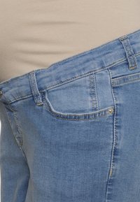 Jeans de ganga azul claro com um design padrão de cinco bolsos, costura visível e uma textura ligeiramente desgastada. Sem detalhes de hardware visíveis.