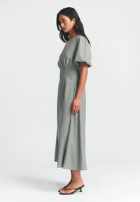 Graues Midi-Kleid mit puffärmel, runder Ausschnitt und tailliertem Schnitt. Glatter Stoff mit einem fließenden Rock und minimalistischer Gestaltung.