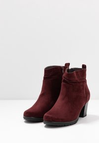 Burgundowe zamszowe botki za kostkę z okrągłym noskiem, zamkiem z boku i solidnym czarnym obcasem. Posiadają subtelny wzór stębnowania na cholewce.