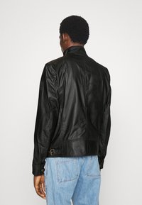 Černá kožená bunda s elegantním designem, vysokým límcem a viditelným šitím. Má boční přezku a hladkou texturu.