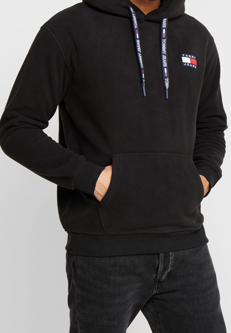 Felpa nera con cappuccio realizzata in tessuto morbido, dotata di tasca frontale, coulisse regolabile con logo e una piccola patch con logo sul petto.