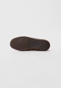 Talpa unei pantofi maro cu un model texturat circular și găuri curbe pe un fundal alb simplu.