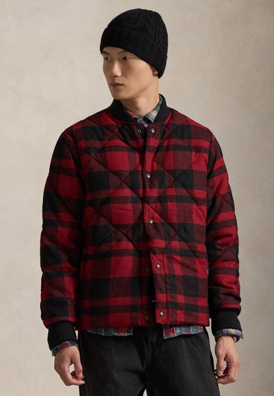 Veste matelassée à carreaux rouges et noirs avec boutons-pression, poignets côtelés et un bonnet en maille foncée. Superposé à une chemise à carreaux.
