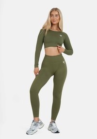 Olivenfarbene Sportbekleidungsset mit langärmligem Crop-Top und hoch sitzenden Leggings, ausgestattet mit geripptem Material und einem weißen Logoakzent.