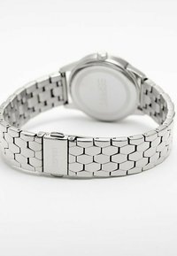 Orologio in metallo argento con bracciale a maglie esagonali e cassa rotonda. Il retro è liscio con un logo impresso. Design e finitura minimalisti.