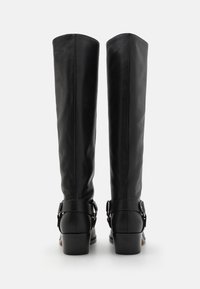 Bottes noires en cuir jusqu'au genou avec une texture lisse, dotées de boucles réglables à la cheville et d'un talon bas et carré.