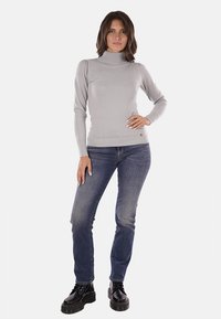 Maglione grigio a collo alto con design aderente, polsini a coste e un piccolo logo. Abbinato a jeans dritti blu scuro e stivali neri.