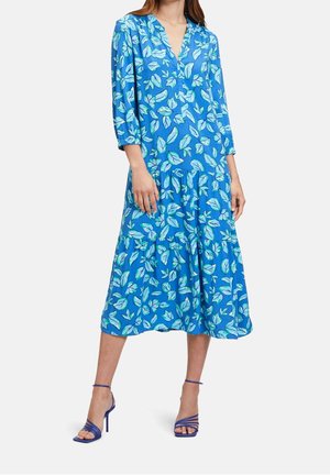 Vrouw draagt een blauwe midi-jurk met een lichtblauwe bloemprint, driekwartmouwen, een v-hals en blauw gestripte hoge hakken sandalen.