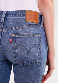 Blå denimjeans med hög midja, med en läderlogotyp, röd etikett och bakfickor med detaljerad och böjd sömnad.