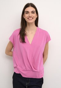 Rosa kortärmad topp med V-ringning och draperade detaljer framtill, tillverkad av lätt fabric, snyggt kombinerad med mörka jeans.