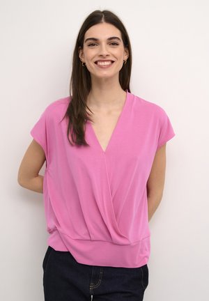 Pink short-sleeve top with a V-neck and draped detailing at the front, made of lightweight fabric, paired with dark jeans.