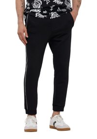 Joggers neri a sigaretta con dettagli laterali a striscia bianca, polsini elasticizzati, due tasche frontali e una texture in tessuto morbido. Abbinati a sneakers bianche.