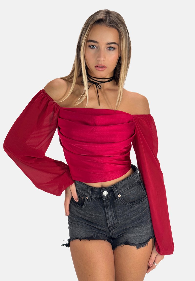 Crop top rouge à épaules dénudées avec un devant froncé, des manches longues en tulle, et une coupe ajustée assorti à un short en denim noir taille haute.