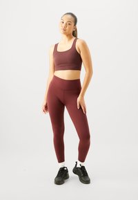 Burgunder sports-bh og leggings sett, tettsittende design, elastisk materiale, glatt tekstur, kombinert med svarte joggesko og hvite ankel sokker.