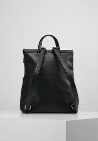 Černý kožený batoh s nastavitelnými popruhy, strukturovaným designem a stříbrnými kovovými detaily. Hladká textura a minimalistická estetika.