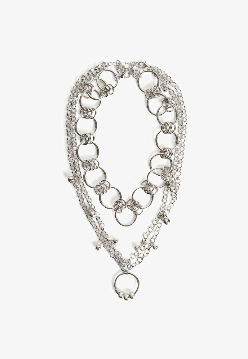 Stříbrný vícevrstvý náhrdelník se vzájemně propojenými kovovými kroužky, malými zvonky a různými texturami řetízků. Doplňky zahrnují hladké a texturované články.