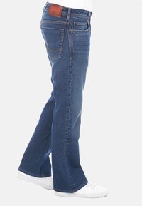 Jeans de denim azul con un diseño de pierna recta, que presentan bolsillos cosidos y una etiqueta de cintura de cuero marrón. Zapatillas blancas completan el look.