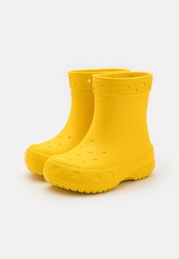 Par de botas de lluvia de goma amarillas brillantes con bordes texturizados y perforaciones, diseñadas para el uso exterior impermeable.