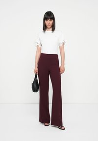 White t-shirt with flared lace sleeves and maroon wide-leg trousers. Black handbag and sandals complete the outfit.