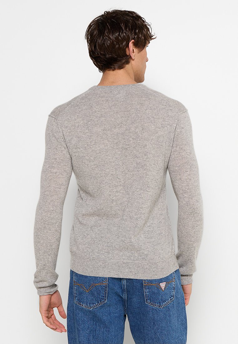 Grauer Strickpullover mit rundem Ausschnitt, langen Ärmeln und gerippten Bündchen. Der Stoff wirkt weich und strukturiert, kombiniert mit blauen Jeans.