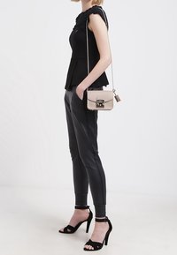 Černý peplum top s texturovaným detailem na ramenou, spárovaný s těsnými černými kalhotami a černými sandály na vysokém podpatku, doplněný béžovou krosnou.