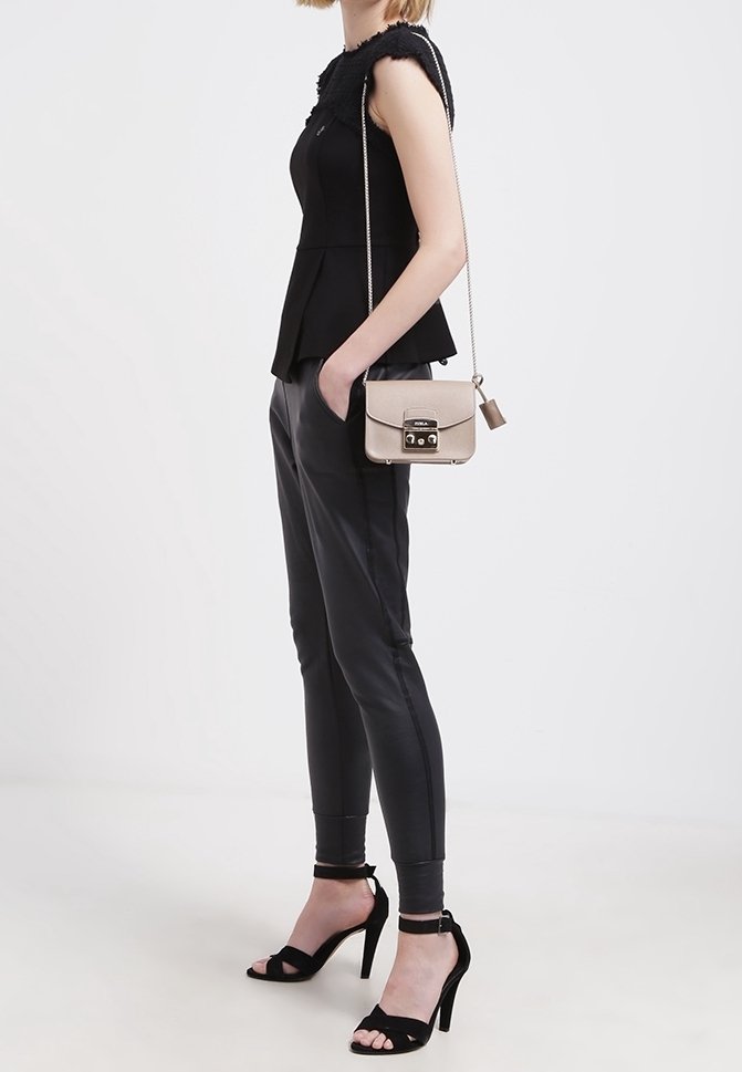 Černý peplum top s texturovaným detailem na ramenou, spárovaný s těsnými černými kalhotami a černými sandály na vysokém podpatku, doplněný béžovou krosnou.