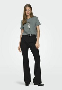 T-shirt grigio a maniche corte con un design di piuma in paillettes e la scritta "Goditi il Viaggio", abbinato a pantaloni neri a vita alta.