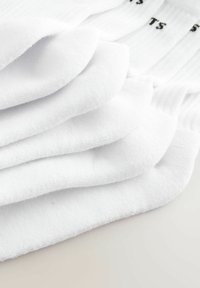 Chaussettes blanches en coton empilées, avec une texture douce et un design de bord-côte. Chaque chaussette comporte un texte noir indiquant la taille ou la marque.