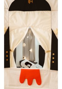 Gyermek játszó színház krémszínű szövetfüggönnyel, fekete díszítésekkel, arany gombokkal és az alján piros kéz formájú részlettel.