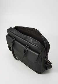 Sac en cuir noir avec texture tissée sur l'avant, fermeture à glissière supérieure, poignées doubles et bandoulière amovible. Intérieur doublé en tissu.
