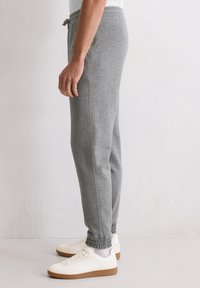 Szare spodnie dresowe z miękkiej tkaniny, wyposażone w elastyczny pas i mankiety. Wzdłuż bocznych szwów widoczne są kontrastowe przeszycia.