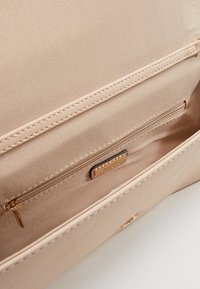 Interno di borsa sintetica rosa chiaro con una tasca con zip, due scomparti aperti e dettagli in hardware color oro. Texture liscia.