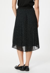 Schwarzer, plissierter Rock mit weißen Punkten, transparentem Stoff, elastischem Bund und Midi-Länge, kombiniert mit schwarzen Loafers.