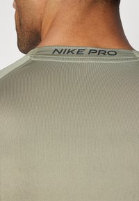 Nike Pro tettskjorte i lys grønn med en glatt tekstur, som har mørk merkevarelogo på baksiden av nakken og flate sømmer.