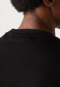 Schwarzes T-Shirt aus weichem Stoff mit Rundhalsausschnitt. Verfügt über ein kleines, geprägtes "Morato"-Logo nahe dem hinteren Kragen.
