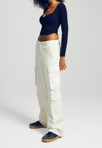 Svart ribbat långärmat topp matchad med krämfärgade cargo-byxor med sidofickor och mörka sneakers med gummisulor.