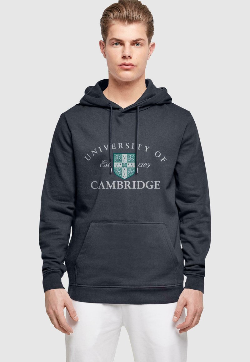 Dark grey hoodie featuring "University of Cambridge" text, a shield logo, front pocket, and adjustable drawstring hood. Soft fabric texture.