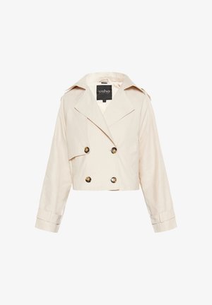 Rövidített bézs zakó, amely pamutból készült, dupla gombolású elülső résszel, nagy gombokkal és széles hajtókákkal, valamint hosszú ujjakra van tervezve.