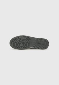 Semelle de chaussure noire en caoutchouc avec des motifs de traction circulaires et linéaires, présentant un emblème central surélevé et des bords latéraux texturés.