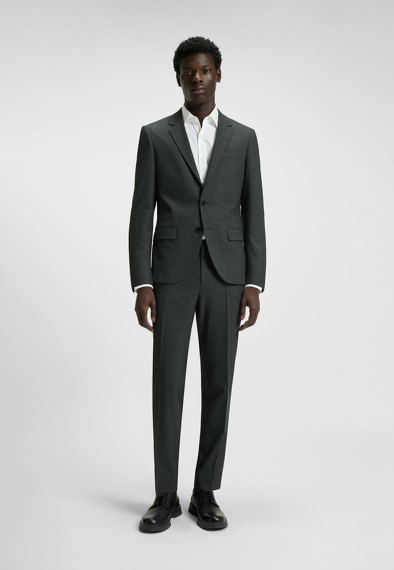 Dunkelgrauer Anzug mit tailliertem Schnitt, einreihigem Blazer, weißem Hemd und schwarzen Schnürschuhen. Hat eine glatte Oberfläche und eine strukturierte Silhouette.